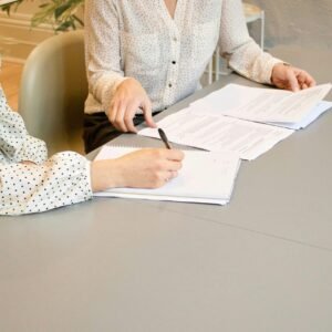 woman signing on white printer paper beside woman about to touch the documents